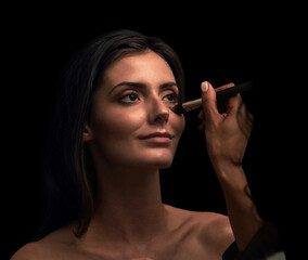 Woman, hand and apply makeup in studio with brush, beauty cosmetics and facial glow of transformation. Girl, tools and artist for foundation, skincare treatment and aesthetic style on dark background