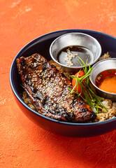Teriyaki Grilled Bangus Belly Rice Bowl with Dipping Sauce isolated on orange background closeup side view of fast food meal