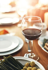 Closeup, glass and wine on table at dinner, restaurant or house for celebration, holiday or party. Red wine, alcohol and vegetables in dining room for thanksgiving, Christmas or fine dining in home