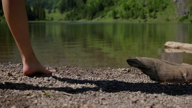 Slow motion shot of sexy legs and barefoot feet at rocky shore of lake in mountains. Close up low angle.