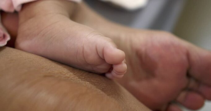 Close-up shot of a newborn baby's tiny foot while she is sitting on her mother's lap.