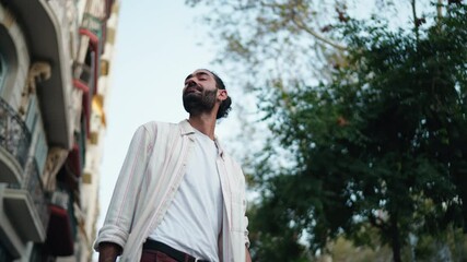 Man standing on city street, looking around while holding his phone, as if checking for updates or searching for friend. His casual posture and urban backdrop, anticipation and social connection

