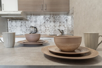 Fototapeta premium design of modern beige kitchen. brown dishes on kitchen table. Plates of different sizes and ceramic mugs. Setting table for breakfast, lunch or dinner. cozy evening at home. Breakfast for two.