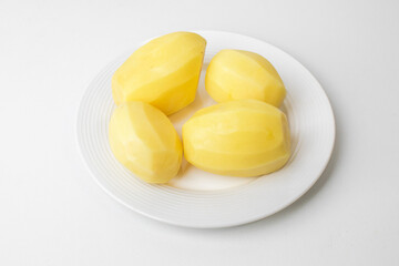 Four peeled potatoes on a white plate symbolize simplicity in cooking, ideal for Thanksgiving meal preparations or family dinners
