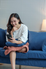 Obraz premium Attractive Asian businesswoman relaxing on the sofa Use your smartphone to surf the Internet. work online at home and happily order online.
