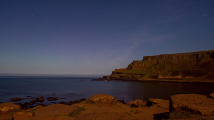 Giant's Causeway with the amphitheatre in the background under a clear night sky, faint green and red hues on the horizon
