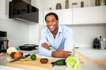 Man smiling in kitchen with fresh vegetables on cutting board
