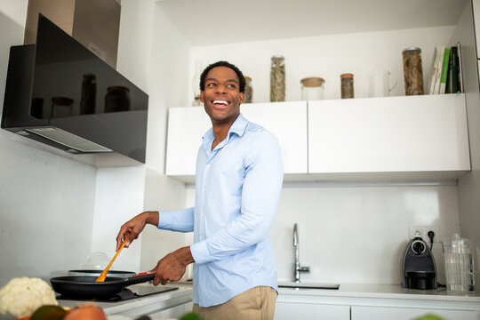 Man smiling while cooking in modern kitchen with frying pan