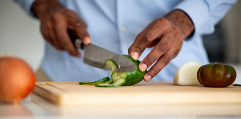 Close-up of hands slicing cucumber on wooden cutting board