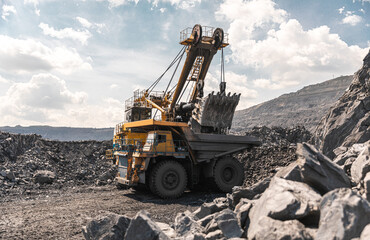 Large quarry dump truck and excavator. Big mining truck work coal deposit. Loading coal into body truck. Production useful minerals. Mining mining machinery to transport coal from open-pit production