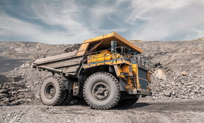 Large quarry dump truck. Big yellow mining truck at work site. Loading coal into body truck. Production useful minerals. Mining truck mining machinery to transport coal from open-pit production