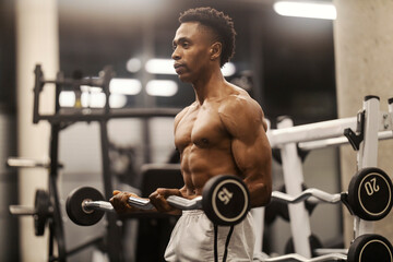 Muscular strong black bodybuilder doing biceps curls with barbell.