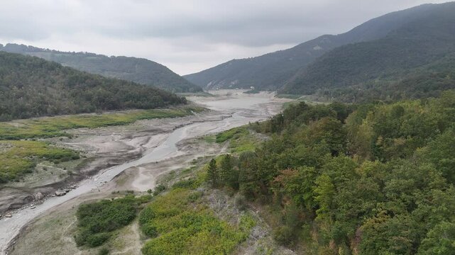 Arda dry riverbed winding through Tolla valley between green hills on a cloudy day in Lago di Mignano, PC, Italy
