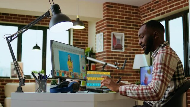 Male african american designer works with photo editing software in his creative workspace at home. Using dual monitors to ensure productivity and innovation in the graphic design world. Camera A.