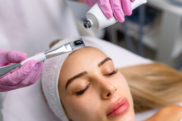 cosmetologist applying black mask on pretty woman face wearing black gloves, gorgeous woman in spa...