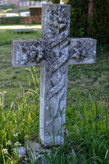 Weathered grey stone cross with engraving in old churchyard surrounded by green grass.