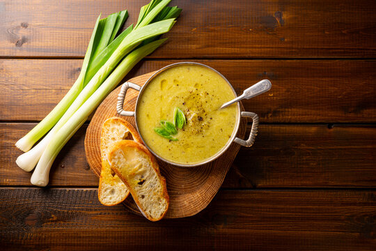 Abowl of leek soup with toasted bread on wooden background top view