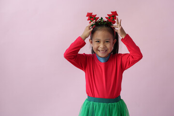 Adorable little Asian girl with Christmas tree headband, antlers showing various poses, standing, smiling, laughing, having fun in various poses, pink background. Holiday concept annual festival.