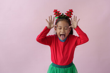 Adorable little Asian girl with Christmas tree headband, antlers showing various poses, standing, smiling, laughing, having fun in various poses, pink background. Holiday concept annual festival.