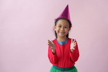 Adorable little Asian girl with a party hat showing various action poses, standing, smiling, dancing, laughing, and having fun in various poses, pink background. Holiday concept annual festival.
