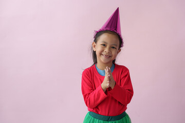 Adorable little Asian girl with a party hat showing various action poses, standing, smiling, dancing, laughing, and having fun in various poses, pink background. Holiday concept annual festival.