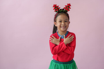 Adorable little Asian girl with Christmas tree headband, antlers showing various poses, standing, smiling, laughing, having fun in various poses, pink background. Holiday concept annual festival.