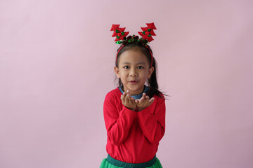 Adorable little Asian girl with Christmas tree headband, antlers showing various poses, standing, smiling, laughing, having fun in various poses, pink background. Holiday concept annual festival.