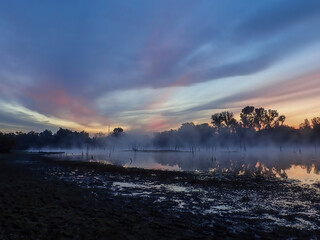 Colorful sky at sunrise with sun rays in the morning fog over the water