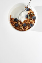 Overhead View of Breakfast Bowl with Greek Yoghurt, Homemade Granola, Nuts and Grapes on White Table.