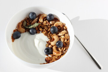 Healthy Breakfast. Greek Yoghurt with Fresh Granola, Nuts, Grapes Served in White Bowl, Teaspoon on White Background.