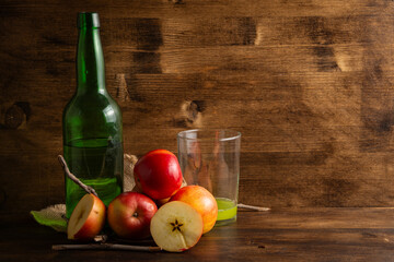 View of bottle and glass with natural cider on table and wooden background with apples, horizontal with copy space