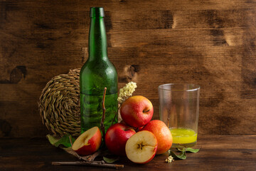 Close-up of bottle and glass with natural cider on table and wooden background with apples, leaves in horizontal with copy space