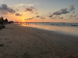 Sunset over a sandy beach with people walking towards the ocean