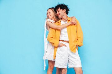 Happy beautiful romantic teenage couple. Smiling handsome caucasian man and young woman in summer clothes posing in studio, hugging sharing emotions, cheerful and happy. Isolated on blue