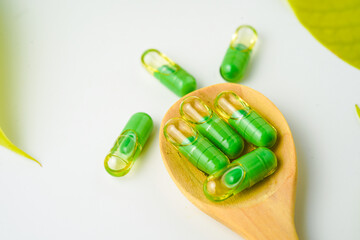 transparent capsules pills with a mixture of green powder and oil in wooden spoon, vitamin supplements