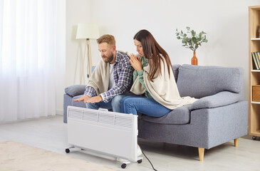 Family couple near heater on couch at home freezing in cool flat in blanket shivering tremble with...