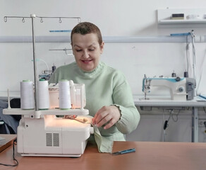 In a sewing studio, a woman sits at a sewing machine and sews clothes from fabric.