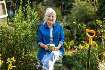 Senior woman relaxing in her garden with a cup of tea in her hand
