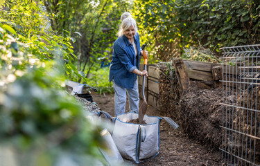 Senior woman shoveling compost heap in her garden
