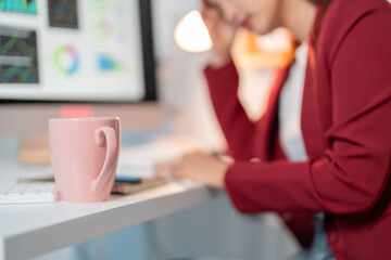 Stressed businesswoman with headache at desk, overwhelmed by work. Computer shows financial data,...