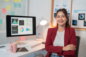 Young professional woman is smiling while sitting at her desk with her arms crossed. She is in her...