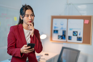 Young asian businesswoman in a modern office, deep in thought with a smartphone, exudes professionalism and success, ideal for concepts of entrepreneurship and strategic thinking