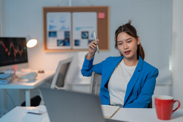 Focused young businesswoman working late at cluttered desk, immersed in technology and finance,...