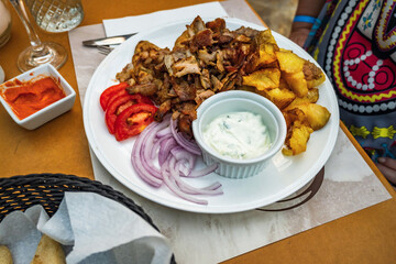 Gyros pork piece with fried potato and vegetable on plate, tzatziki.