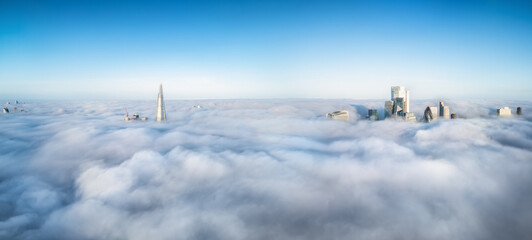 Elevated, panoramic view of the skyline of London, England, during fog with only the tips of the...
