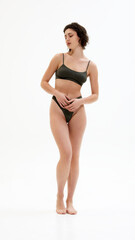 Fototapeta premium Confident young and fit woman in dark green minimalist underwear set strikes relaxed pose. Effortless style and grace. Concept of spa procedure, self-care treatments, self-love, fashion and style. Ad
