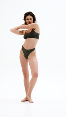 Full-length photo of young attractive woman posing in dark green lingerie and looking at camera,...