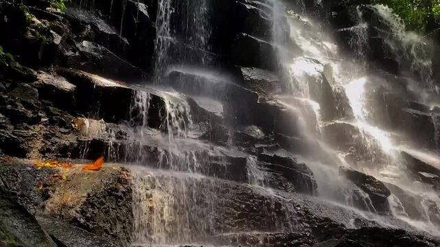 Beautiful Kanto Lampo Waterfall cascading over rocky steps, surrounded by lush greenery in Bali, static view of light shimmering on water