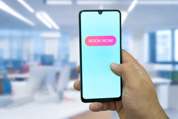 Close-up of the “Book Now” message on the smartphone screen. Online booking concept. Office background. Early booking message. 