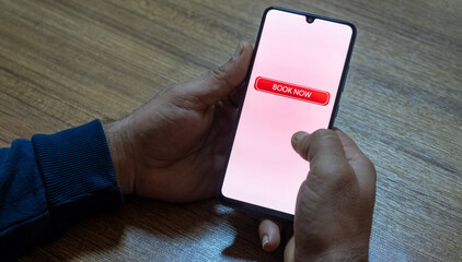 Close-up of the “Book Now” message on the smartphone screen. Online booking concept. Office background. Early booking message. 